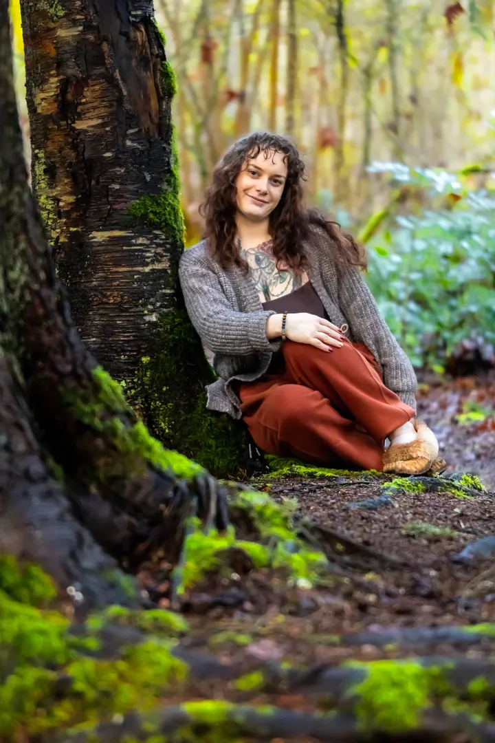 Olivia Greenland standing in forest light, holding herself during self portrait photography session.